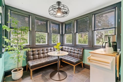 A cozy nook with a black leather banquette, round glass table, and a tall indoor plant, illuminated by natural light.