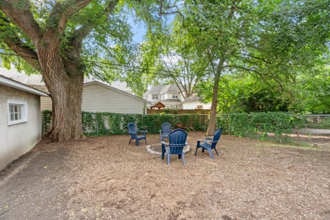 Backyard setting with a fire pit and blue chairs under a tree.