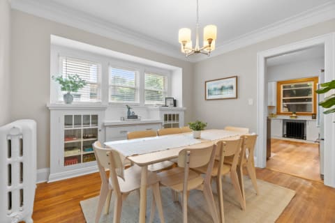 A dining room featuring a wooden table, light-colored chairs, and natural light from large windows.
