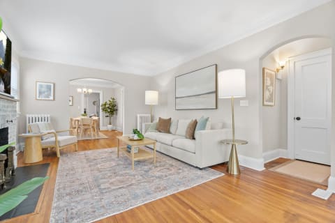 A living room with a cream sofa, abstract artwork, and a dining area in the background.