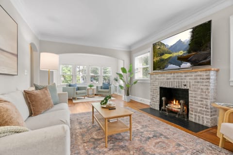 Cozy living room featuring a light gray sofa, teal chairs, and a brick fireplace with a TV overhead.
