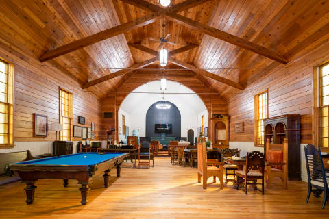 A spacious game room with a billiards table, vintage wooden furniture, and a vaulted wooden ceiling.