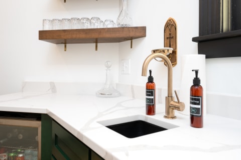 Modern bathroom counter with marble surface, brass faucet, and amber bottles.