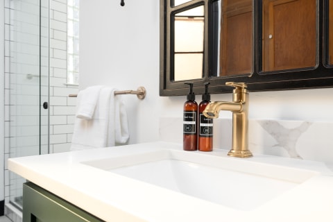Modern bathroom sink with a gold faucet, hand soap, and lotion bottles on a white countertop.