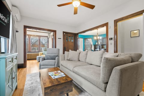 Cozy living room featuring a light gray sectional sofa and wooden accents, with teal walls visible in the adjoining dining area.
