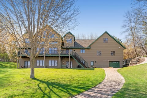 A large two-story home with green accents, set on a green lawn with a pathway leading to it.