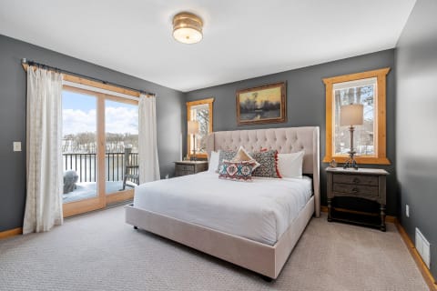 Elegant bedroom with a tufted bed, decorative pillows, and large windows revealing a snowy landscape.