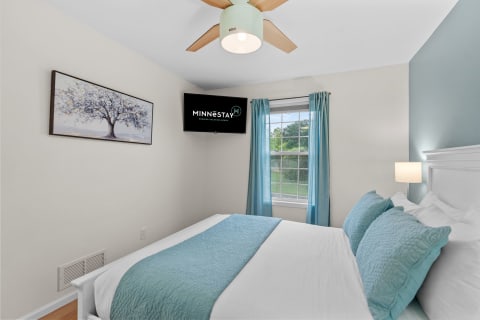 A cozy bedroom with a tidy bed, decorative pillows, and a mounted television.
