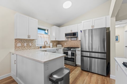 Modern kitchen featuring white cabinets, a large window, and stainless steel appliances.