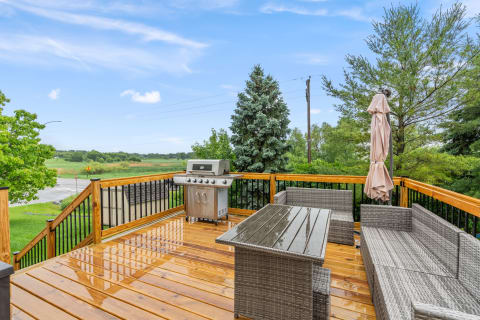 An outdoor deck featuring a dining table, seating area, and barbecue grill, surrounded by greenery.