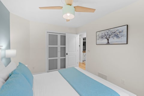 A modern bedroom interior with a bed, blue pillows, and a tree painting on the wall.