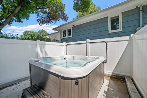 Hot tub in a private outdoor setting, fenced with white panels and trees in the background.