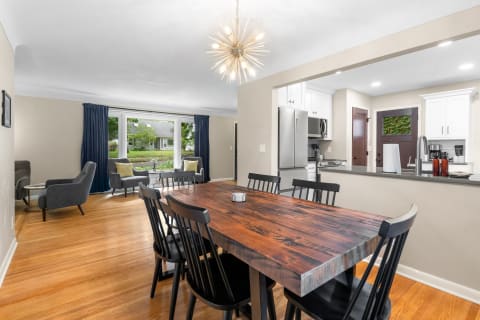 A modern dining area with a rustic wooden table, black chairs, and a view of the garden.
