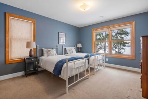 Cozy bedroom with two twin beds, blue walls, and large windows overlooking trees.