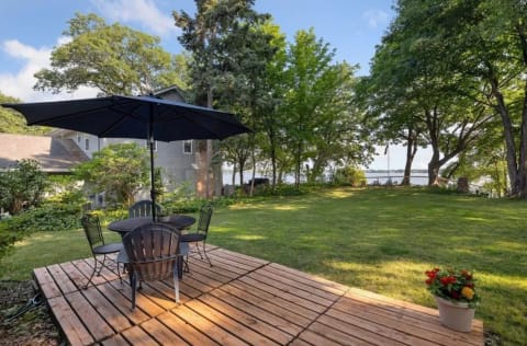 Outdoor deck with table and chairs overlooking a green lawn and water.