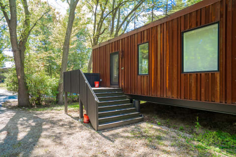 A modern house with rust-colored wood siding and a staircase, set among trees.