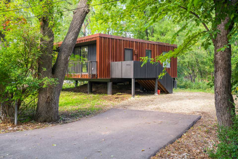 Modern house with elevated structure surrounded by greenery.