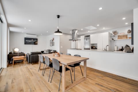 Contemporary open-concept dining room and living area featuring wooden table, black chairs, and modern appliances.