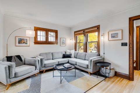 Modern living room featuring a gray sectional sofa, framed artworks, and large windows.