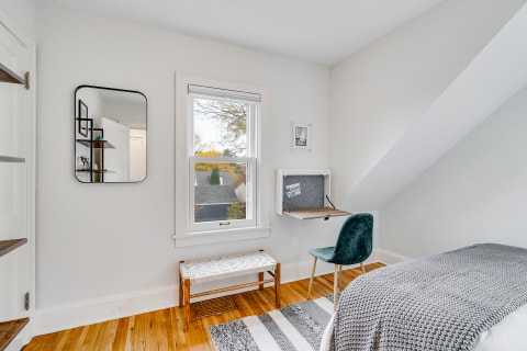 A cozy minimalist room with a mirror, desk, bench, and window allowing natural light in.