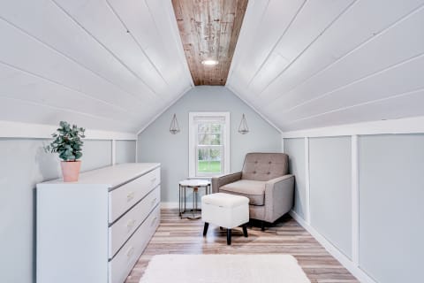 An inviting attic space featuring a gray armchair, white dresser, and soft decor elements.