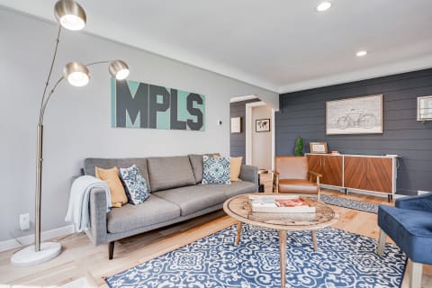 A contemporary living room with a grey sofa, leather armchair, artistic wall decor, and natural wood accents.