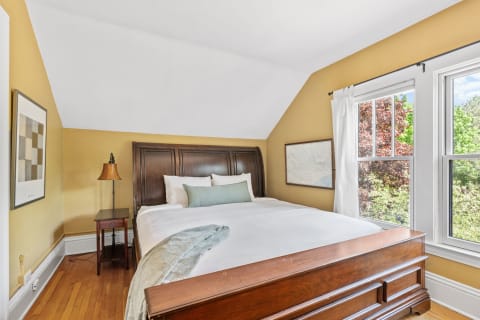 A bright bedroom with yellow walls, wooden bed, and natural light from the window.