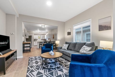 Stylish living room featuring a gray sofa, blue chairs, and a dining area in the background.