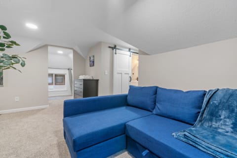 Cozy attic living area with blue sectional sofa and light carpeting.