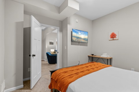 Cozy bedroom with an orange blanket on the bed and a mounted flat-screen TV.