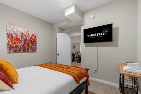 Interior view of a cozy bedroom with a bed, artwork, and a mounted TV.