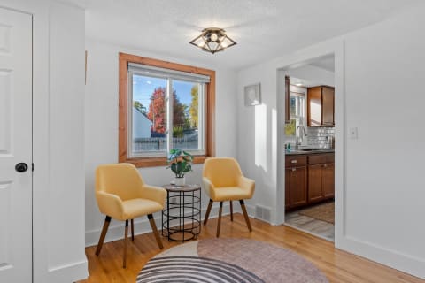A living area featuring yellow chairs and a view of colorful trees through a window.