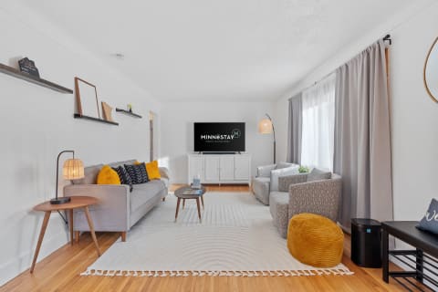 A bright living room featuring a gray sofa, patterned armchairs, and a television mounted on the wall.