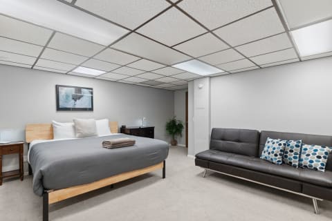 Modern basement bedroom with a queen bed, nightstands, and a sofa with decorative cushions.