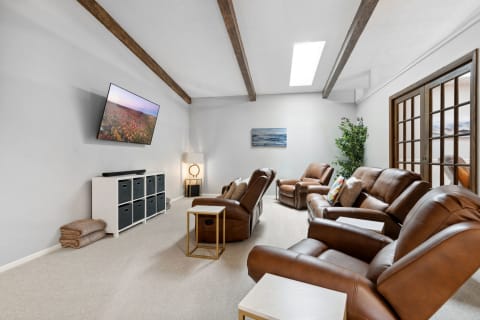 A modern living room featuring recliner chairs, a TV mounted on the wall, and a soft carpet.