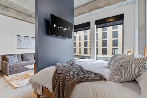 Interior view of a modern studio apartment featuring a bed, sofa, and large windows.