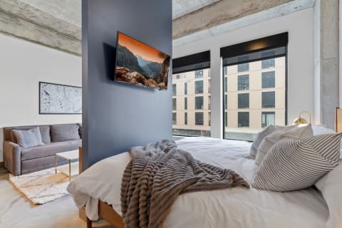 Modern bedroom featuring a gray blanket on the bed, a sofa, and large windows.