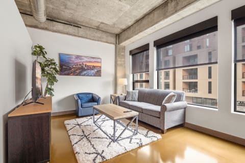 Modern living room with a gray sofa, blue armchair, large windows, and cityscape artwork.