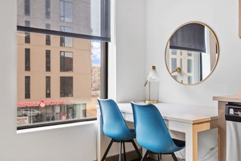 A bright workspace with a white desk and blue chairs beside a window showing a view of a building with a boxing studio sign.