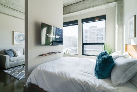 Minimalist bedroom with a bed, television, and a sitting area.