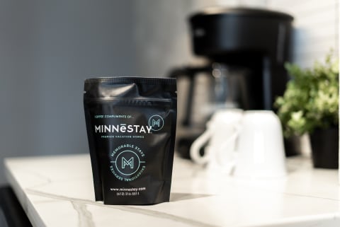 Black coffee bag from MINNESTAY on a marble countertop with a coffee maker in the background.