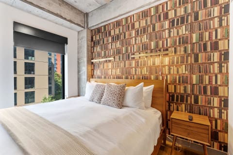Modern bedroom with a bed, book-themed wall, and large window.