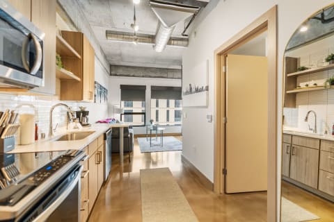 A contemporary kitchen with wooden cabinets, modern appliances, and a living area with large windows.