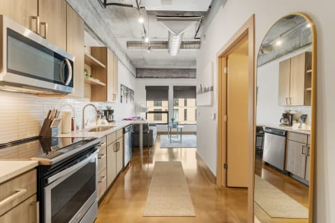 Modern kitchen interior with wooden cabinets and stainless steel appliances, leading to a living space.