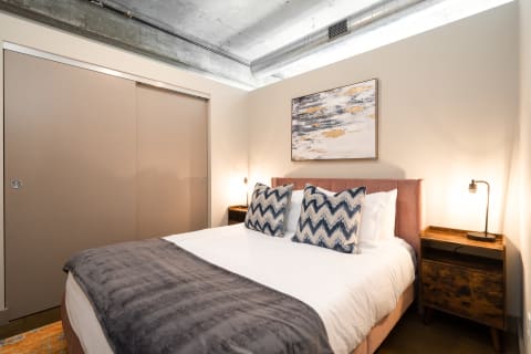 A modern bedroom featuring a pink headboard, decorative pillows, and rustic nightstands.