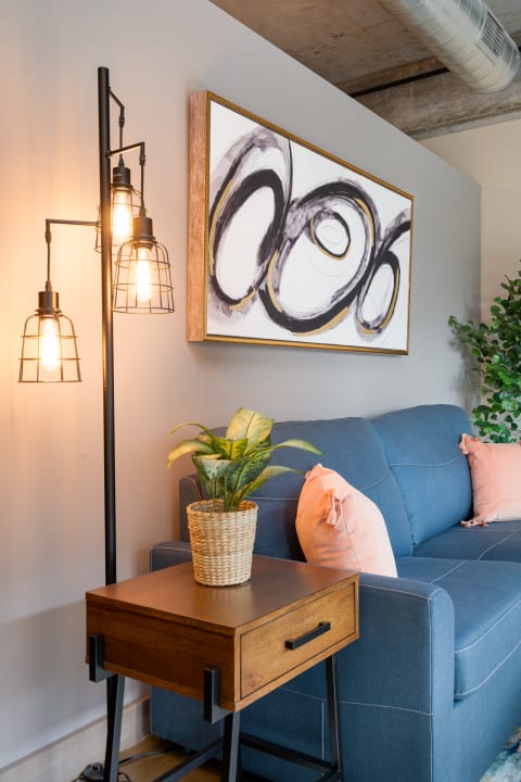 A cozy living room corner with a blue sofa, a wooden side table with a plant, and a modern floor lamp.
