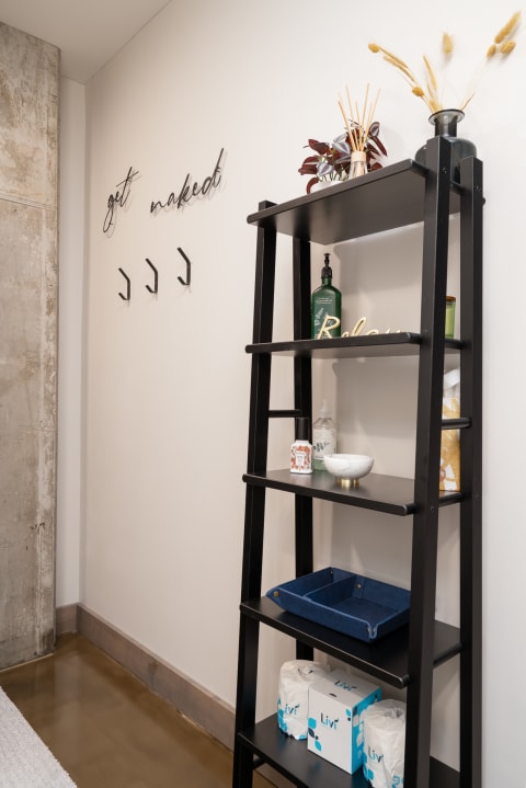 A black ladder shelf with decorative items and a wall with cursive text saying 'get naked'.
