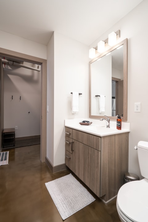 Contemporary bathroom featuring a wooden vanity, white countertop, and a large mirror with frosted glass lighting.
