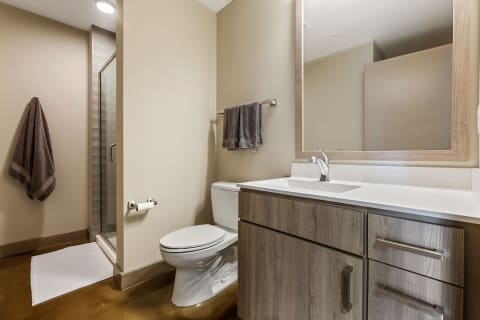 A minimalist bathroom with a white vanity, glass shower, and dark gray towels.