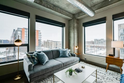 Contemporary living room with grey sofa, floor lamp, and large windows showing a winter cityscape.